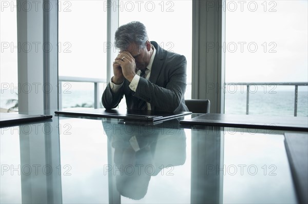 Caucasian businessman holding head in hands at conference table