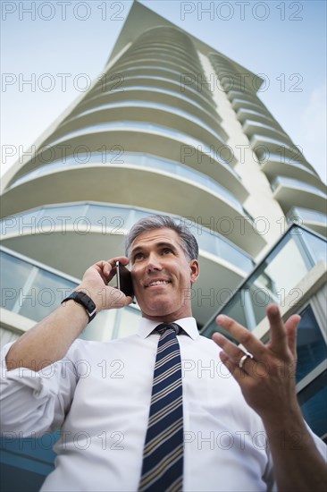 Low angle view of Caucasian businessman using cell phone at high rise building