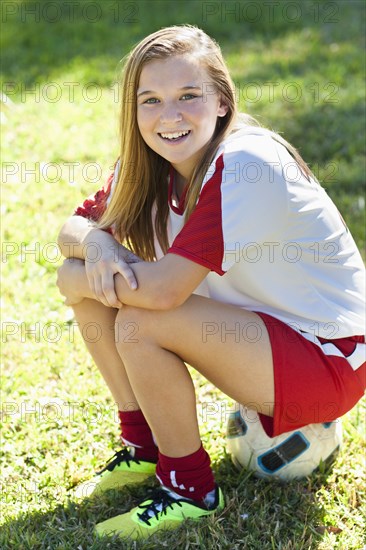 Caucasian soccer player sitting on ball in grass