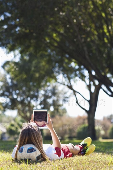 Caucasian soccer player laying in grass using digital tablet