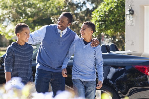 Father hugging sons near car