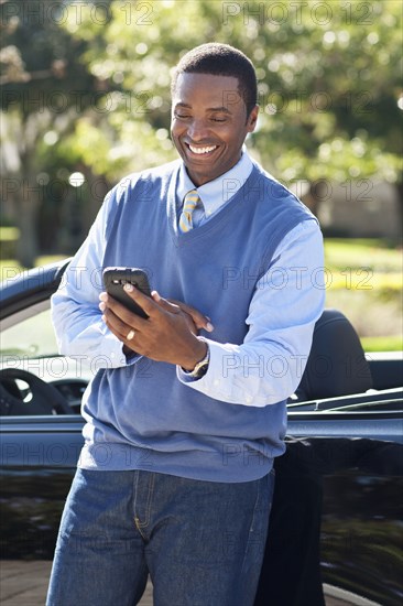 Black man using cell phone at convertible