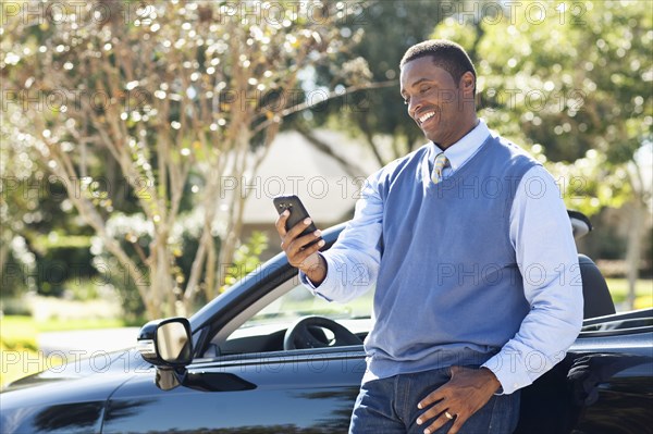 Black man using cell phone at convertible