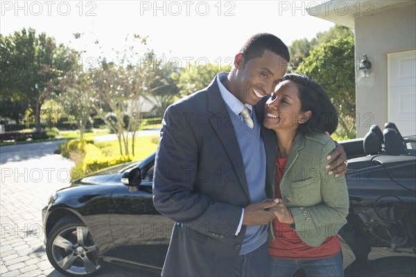 Couple hugging in driveway at convertible