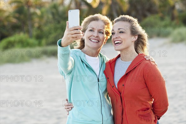 Caucasian mother and daughter taking selfie on beach