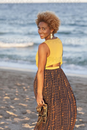 Black woman carrying sandals on beach