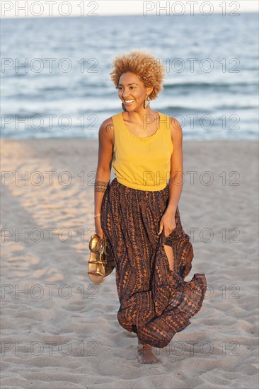 Black woman carrying sandals on beach