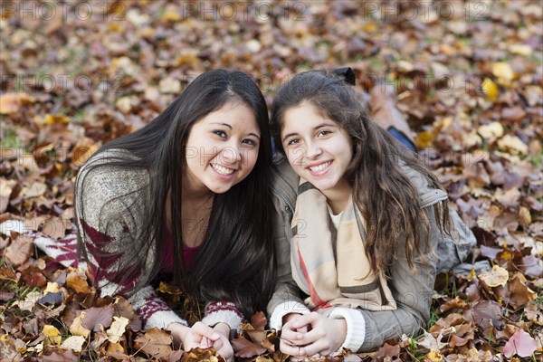 Hispanic sisters laying in autumn leaves