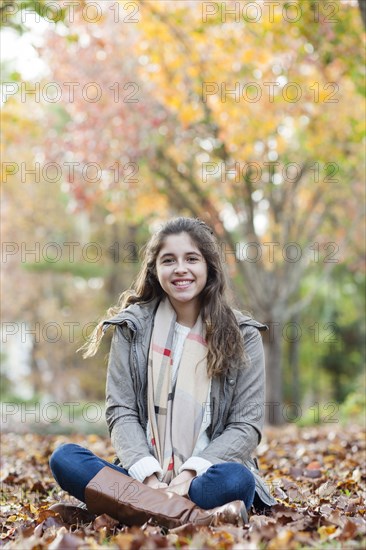 Hispanic girl sitting in autumn leaves