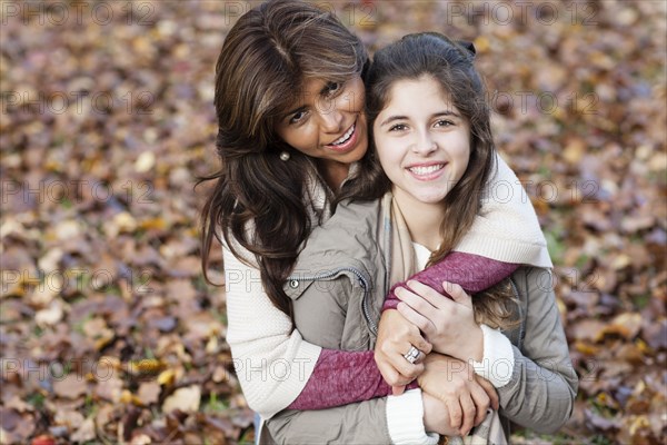 Hispanic mother and daughter hugging in autumn leaves