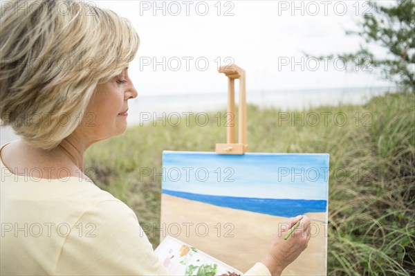 Older Caucasian woman painting beach outdoors