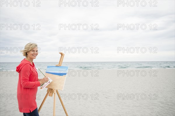 Older Caucasian woman painting on beach