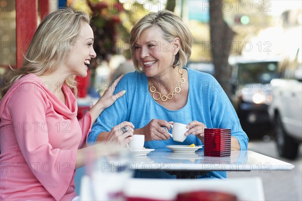 Caucasian mother and daughter drinking coffee at sidewalk cafe