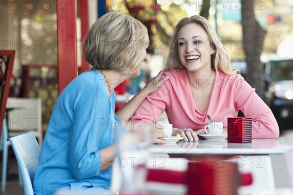 Caucasian mother and daughter drinking coffee at sidewalk cafe