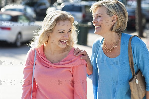 Caucasian mother and daughter walking on city sidewalk