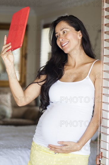 Pregnant Hispanic woman taking selfie with digital tablet