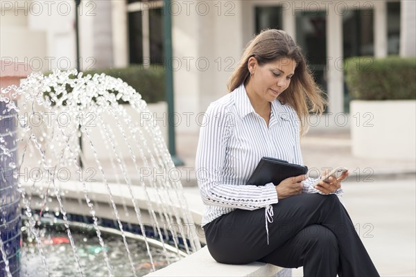 Caucasian businesswoman using cell phone near fountain