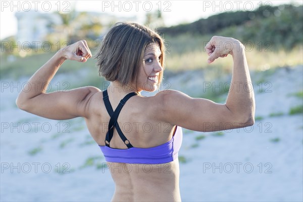 Caucasian woman flexing muscles on beach