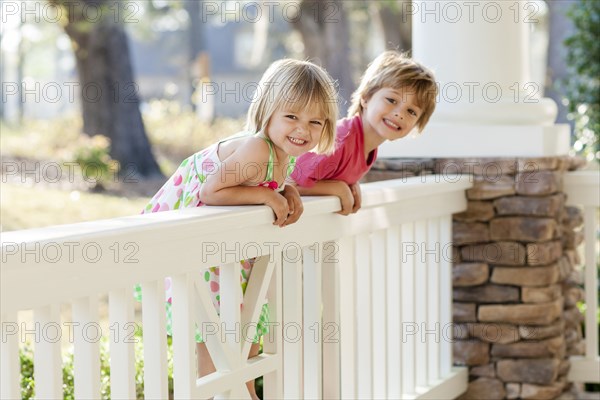 Caucasian brother and sister leaning over porch