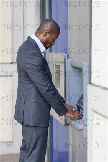 Black businessman using ATM in city