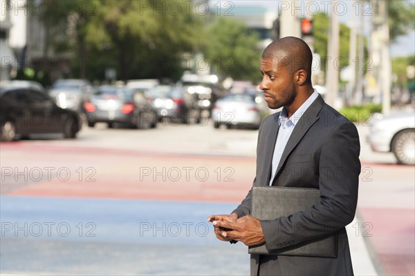 Black businessman using cell phone at crosswalk