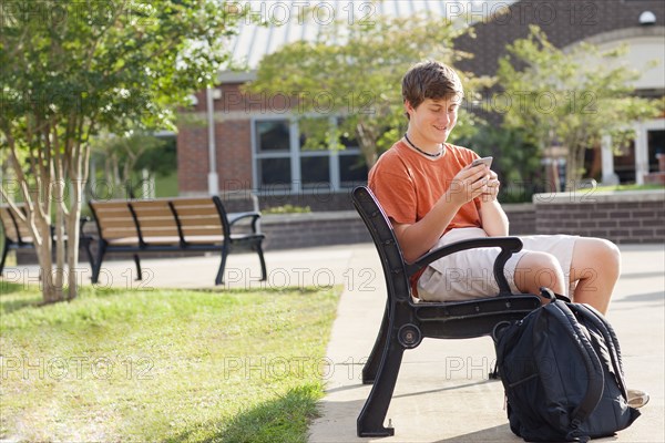 Caucasian teenage boy using cell phone on bench