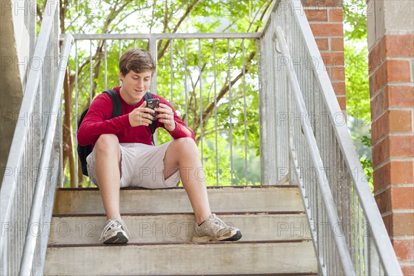 Caucasian teenage boy using cell phone on steps