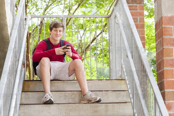 Caucasian teenage boy using cell phone on steps