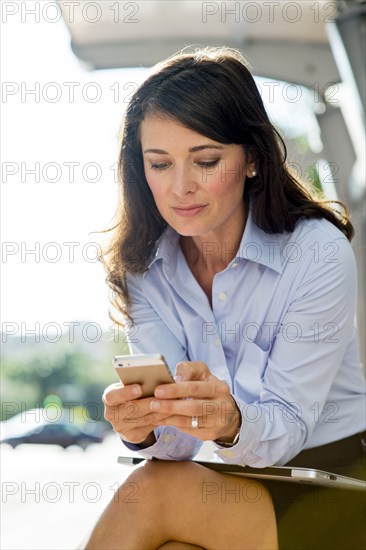 Caucasian businesswoman using cell phone at bus stop