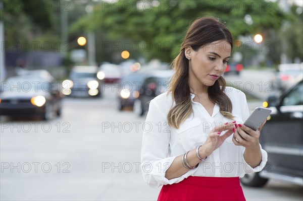 Hispanic businesswoman using cell phone outdoors