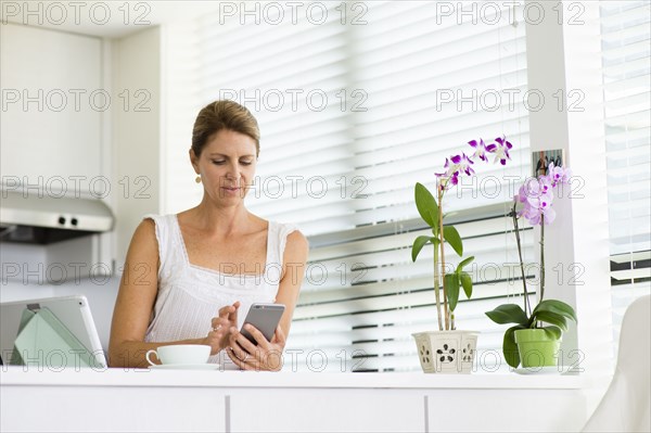 Caucasian woman using cell phone in kitchen