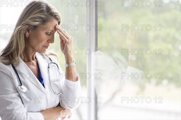 Caucasian doctor rubbing forehead at window