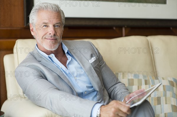 Caucasian man smiling on sofa holding digital tablet