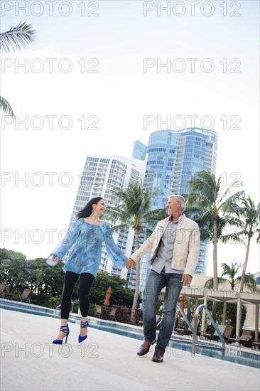 Caucasian couple holding hands near swimming pool