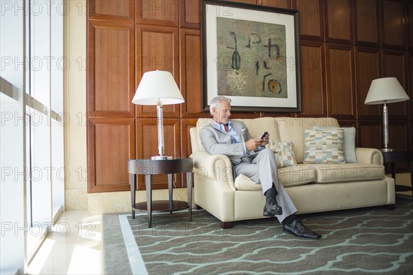 Caucasian man sitting on sofa texting on cell phone