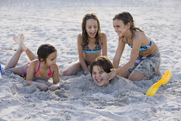 Hispanic girls burying Hispanic boy in sand