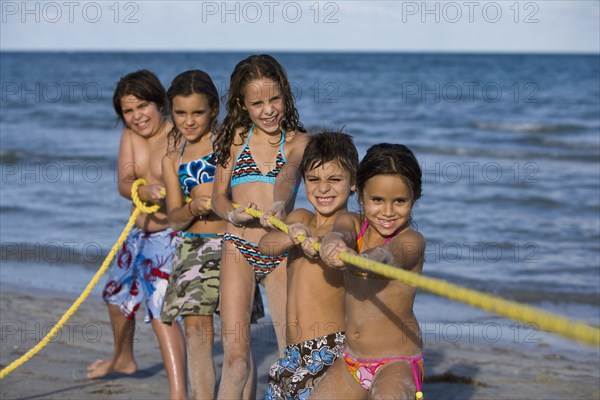 Hispanic children playing tug-of-war on beach