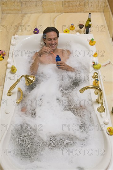 Hispanic man in bubble bath blowing bubbles