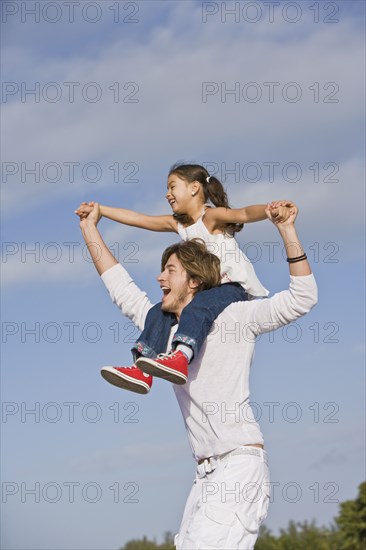 Hispanic father carrying daughter on shoulders