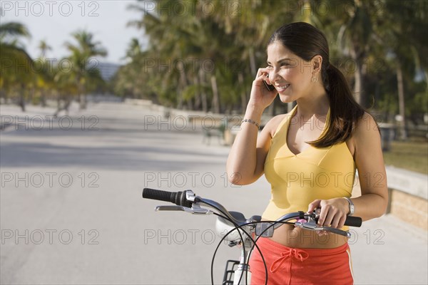 Hispanic woman on bicycle talking on cell phone