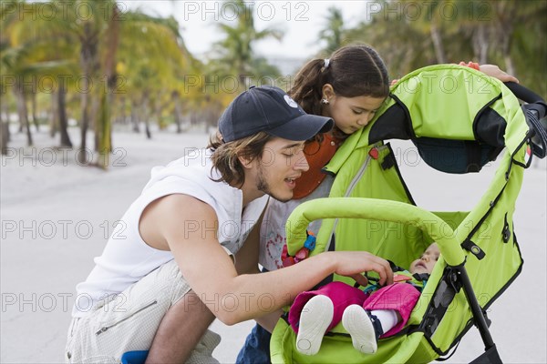 Hispanic father and daughter checking on baby in stroller