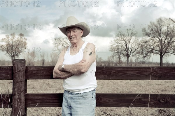 Senior man in cowboy hat standing near wooden fence