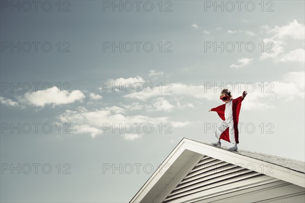 Caucasian boy in cape at edge of roof