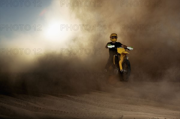 Caucasian man riding dirt bike in dust cloud