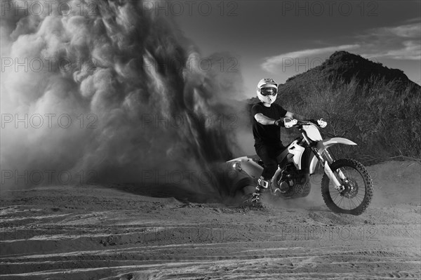 Caucasian man riding dirt bike in dust cloud