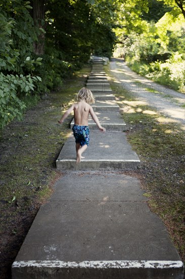 Caucasian boy climbing stairs near rural path