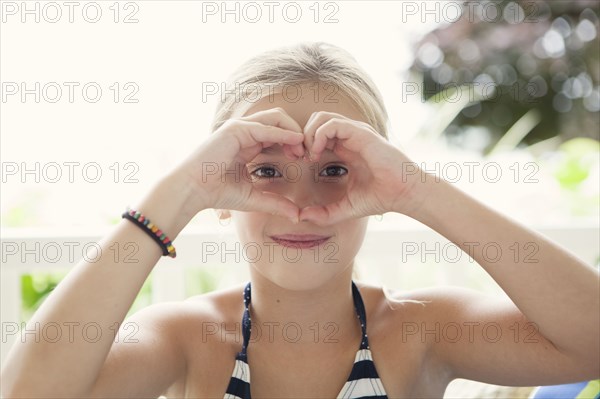 Caucasian girl making heart shape around eyes