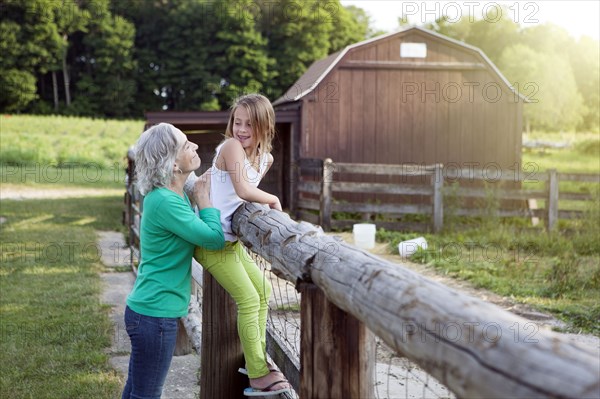 Caucasian grandmother and granddaughter smiling at farm fence