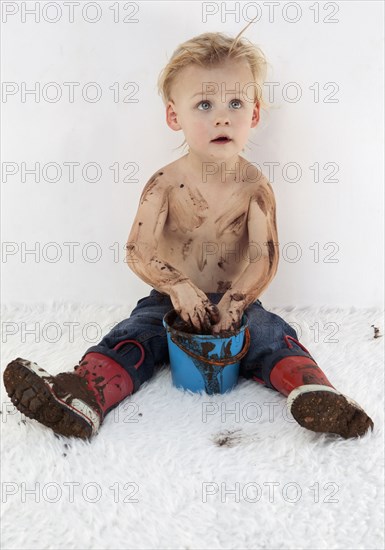 Messy Caucasian boy playing with mud on white carpet