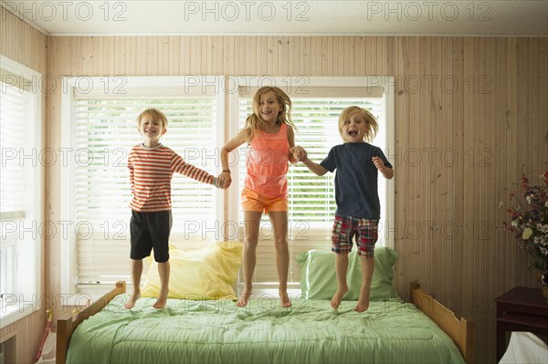 Caucasian children jumping on bed